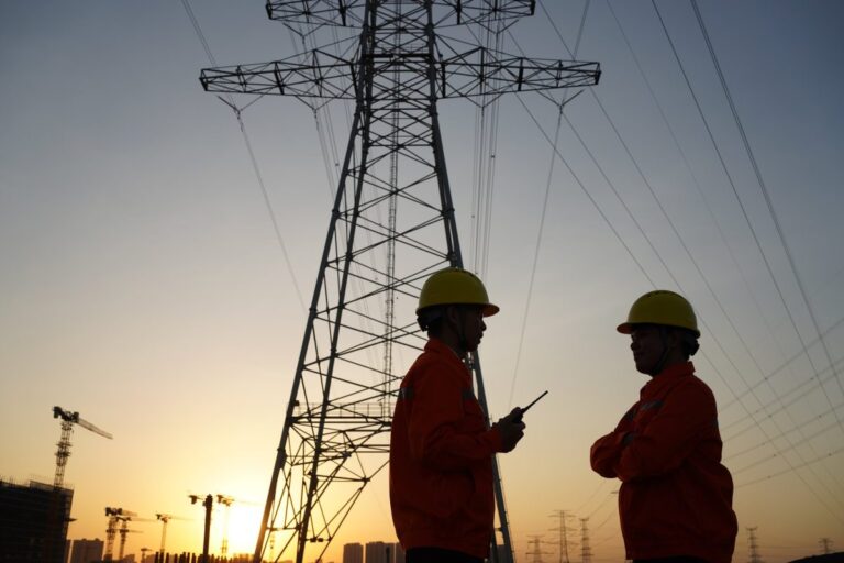 Two workers inspect high-tension power lines.