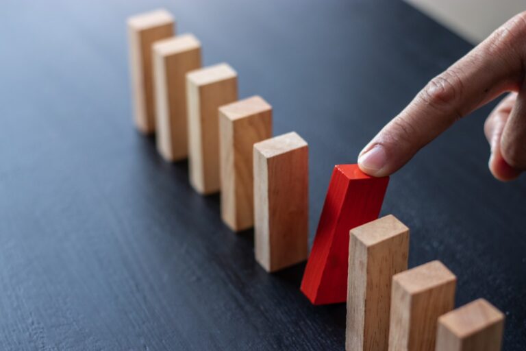 finger pulling red domino block out of row of dominoes