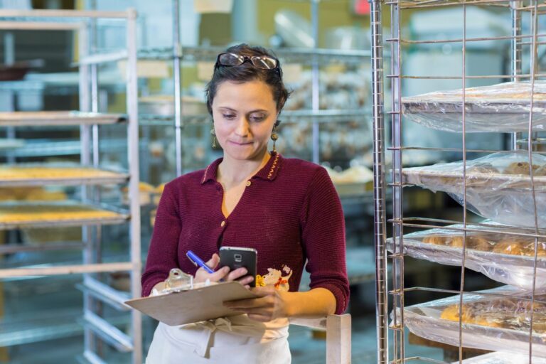 Woman holding clipboard using smartphone in bakery, used in post about Mercu
